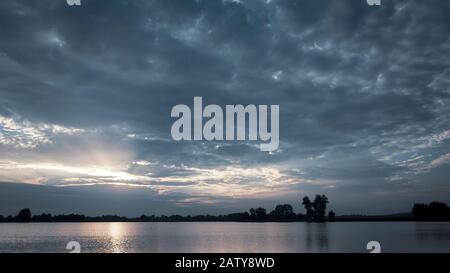 The sun shines through the blue clouds above the water, evening view Stock Photo
