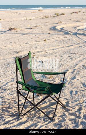 A portable foldable solar panel hangs on a travel chair. Tourist camping in the summer on the seashore. Stock Photo