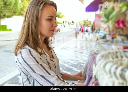 Pretty woman choosing shawl in street shop on vacation. Stock Photo