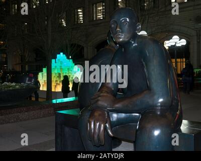 Two Men on a Bench and The Pyramid in Canary Wharf during Winter Lights 2020 in the dark at night Stock Photo