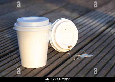 Closeup of two white single-use paper coffee cups with a blank surface on wooden background, outdoors in the morning Stock Photo