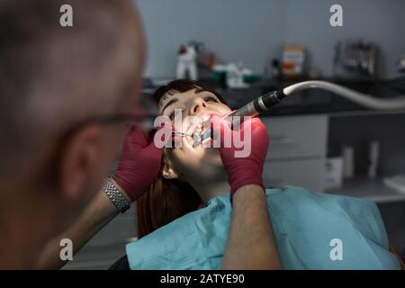 Young female patient takes a dental attendance in the dentist's office, performed by senior man doctor Stock Photo