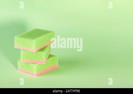 Three green pink kitchen foam sponges on a green background. Sponge for washing dishes and housework. Copy space. Front view. Stock Photo