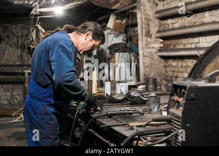 aged male locksmith processes the workpiece using an angle grinder Stock Photo