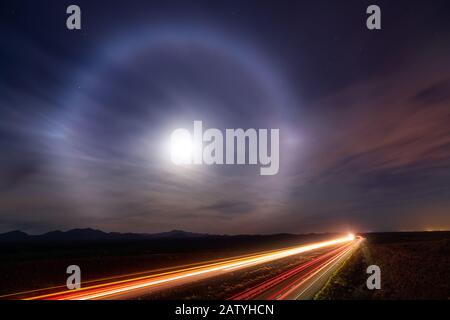 Moon halo in the night sky above car light trails on Interstate 10 near Tucson, Arizona Stock Photo