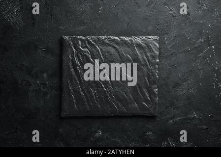 Square black stone dish. On a black stone background. Top view. Free space for your text. Stock Photo