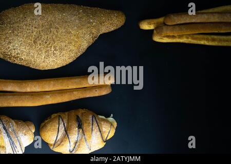 Different types of fresh bread with grain on a black rustic background. bread stands in one vertical row Stock Photo