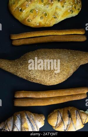 Different types of fresh bread with grain on a black rustic background. bread stands in one vertical row Stock Photo