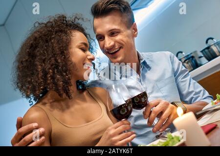 Romantic Date. Young multiethnic couple at home sitting at table eating dinner hugging laughing happy close-up Stock Photo