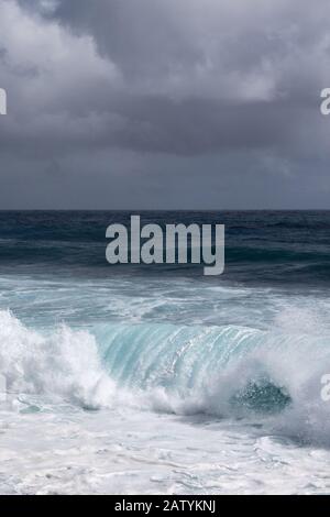 Kaimu Beach, Hawaii, USA. - January 14, 2020: Portrait of Dark ocean under heavy gray rain cloudscape produces white surf when azure wave turns and cr Stock Photo