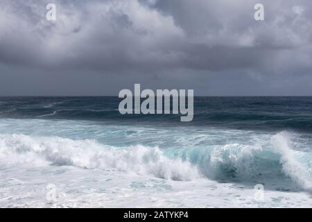 Kaimu Beach, Hawaii, USA. - January 14, 2020: Dark ocean under heavy gray rain cloudscape produces white surf when azure wave turns and crashes. Stock Photo
