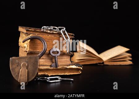 Old books strapping a shiny chain. Prohibited literature open to readers. Dark background. Stock Photo