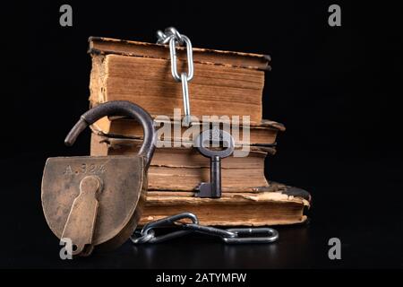 Old books strapping a shiny chain. Prohibited literature open to readers. Dark background. Stock Photo
