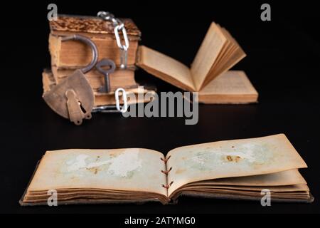 Old books strapping a shiny chain. Prohibited literature open to readers. Dark background. Stock Photo