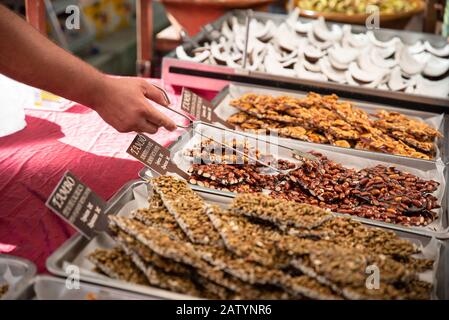 Seller chooses for buyer fried nuts in caramel lying on the tray. Known as gozinaki or gozinaqi. Trading outlet in the summer open-air festival Stock Photo