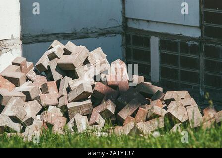 a large pile of gray silicate bricks on the background of green grass and the wall of a residential building. The concept of the beginning of Stock Photo