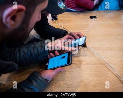 Paris, France - Nov 3, 2017: Overhead view of two Male friends customers admiring inside Apple Store the latest professional iPhone smartphone manufactured by Apple Computers Stock Photo