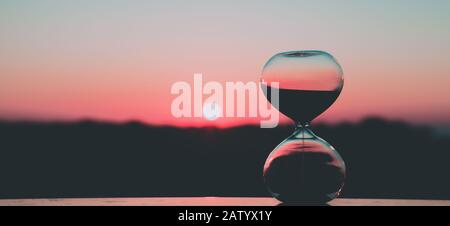 Hourglass against the background of the rising sun and the pink sky, art photography Stock Photo