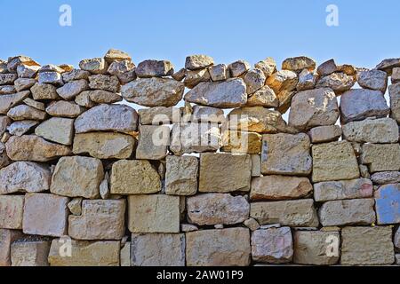 Limestone wall of brickwork with cracked boulders against blue sky background. Natural build texture with copy spac Stock Photo