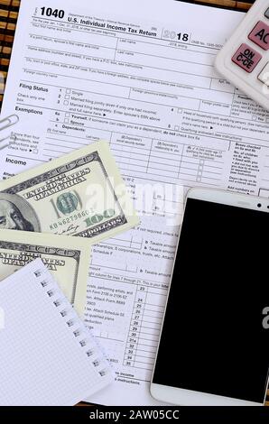Composition of items lying on the 1040 tax form. Dollar bills, calculator, smartphone, paper clip and notepad. The time to pay taxes Stock Photo