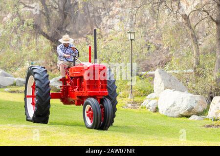 Handsome man with sunglasses driving the tractor to work on the farm Stock Photo