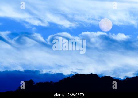 Full Moon is Rising in the Night Sky Over a Surreal Fantasy Like Cloudscape Stock Photo