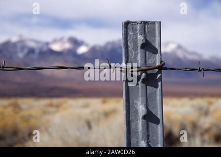 detail of barbed wire fence on metal post with selective focus and defocussed mountains in the distance Stock Photo