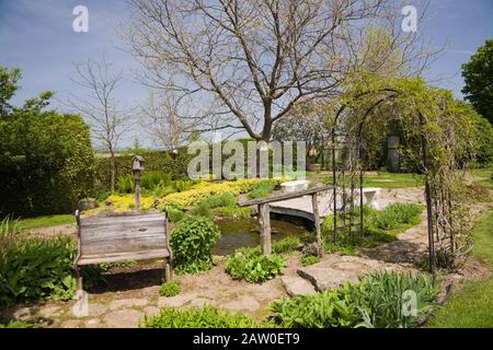 Flagstone path with old wooden sitting bench and black metal arbour in backyard country garden in spring Stock Photo