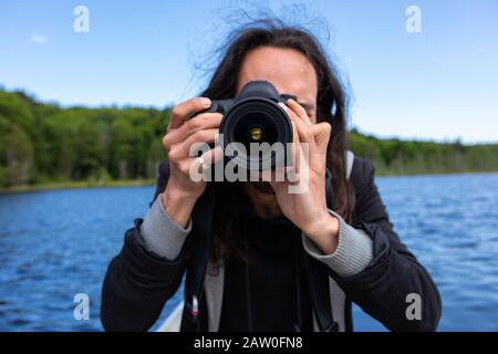 Closeup of young long haired american native man traveling in lake of Northern Quebec, Canada in canoe while taking photos and videos wit DSLR camera Stock Photo