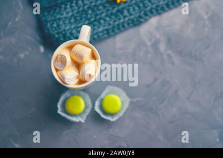 Hot coffee with marshmallow and milk or cream and yellow macaroons on the loft table in a romantic setting with chrysanthemums nearby Stock Photo