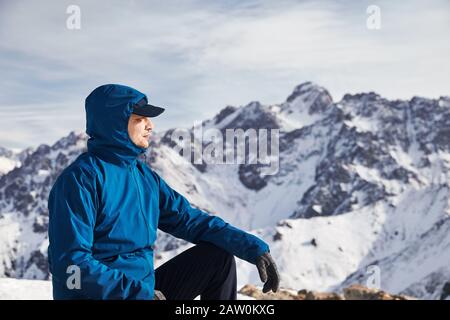 Portrait of happy Asian climber in blue jacket at high snowy mountains. Outdoor climbing and mountaineering concept. Stock Photo