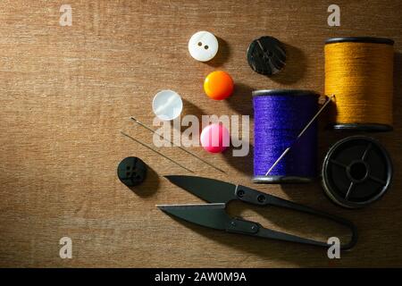 Needle and threads against plastic button and thread cutting scissors on wooden table. Top view and copy space for text. Concept of tailor or Designer Stock Photo