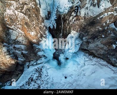 Hiker is walking near frozen waterfall with icicles at snowy mountains in Kazakhstan. Aerial drone shot, top view. Stock Photo
