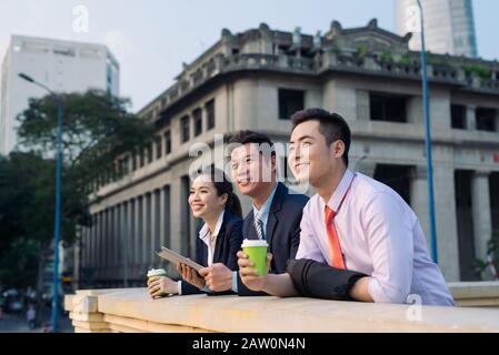 Asian business woman and men having coffee break outside in front of building Stock Photo
