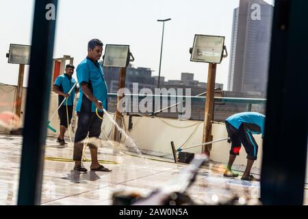 2 November 2019; Dubai, United Arab Emirates; Indian guys in blue uniforms washing the balcony with cleaning tools in Dubai, UAE Stock Photo