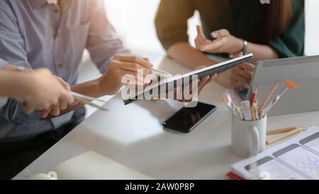 Cropped shot of application developer team using digital tablet while consulting on their UI project in simple co working space Stock Photo