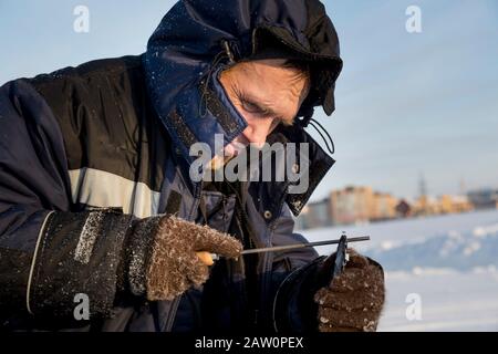 A worker in a blue jacket sharpens a chainsaw chain. Stock Photo