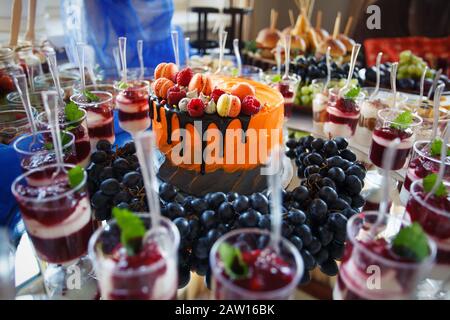 Dessert snacks in cups, fruits, and fruit cakes. Luxury food and drinks on wedding table. Stock Photo