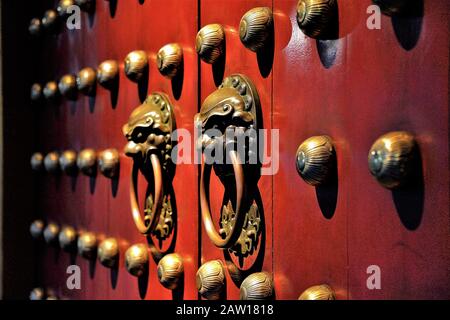 Pair of bronze Chinese Lion head door knockers on red Buddhist temple door in Chinatown Singapore in evening light and perspective view and soft focus Stock Photo