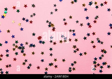 Multicolored confetti or sparkles in the form of small stars on a pink background. Celebration of the holiday. Stock Photo