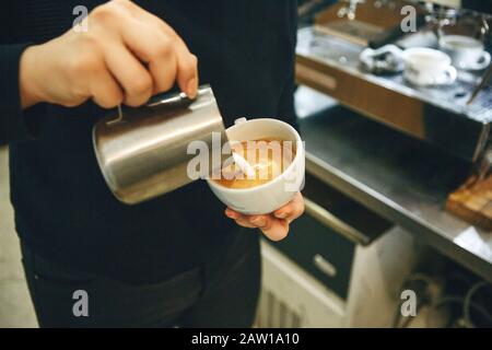 Barista pours milk or cream into coffee and draws a drawing on the foam. Stock Photo
