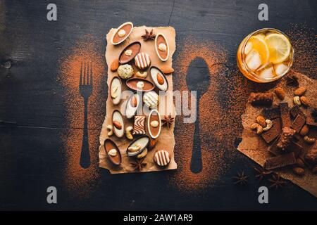 A glass of brandy. Whiskey. Assortment of chocolates. Wooden on the black surface. Top view. Stock Photo