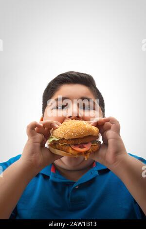 Young boy eating a large burger in hand. (Obesity) Stock Photo