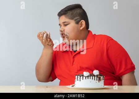 Young boy looking at his hands covered in cake. (Obesity)
