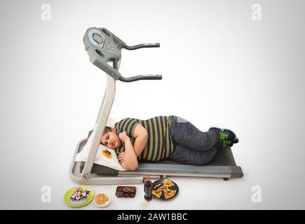 Young boy sleeping on the treadmill with lots of junk food around him. (Obesity) Stock Photo