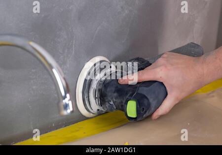 Random-orbit disc sander held in grip of man's hand, refinishing piece of custom sand stucco Stock Photo
