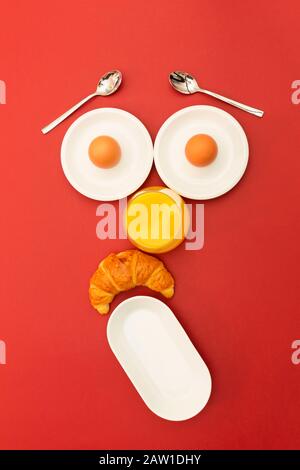 Fun breakfast concept with abstract astonished human face made of breakfast items on red background Stock Photo