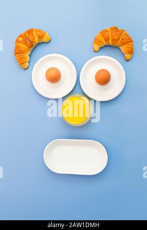 Fun breakfast concept with abstract astonished human face made of breakfast items on blue background Stock Photo