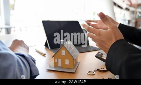 Cropped shot of real estate agent using  blank screen tablet while presenting to customer on wooden table background Stock Photo