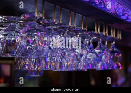 Empty wine glasses hanging over a bar rack in a nightclub. Dark background Stock Photo